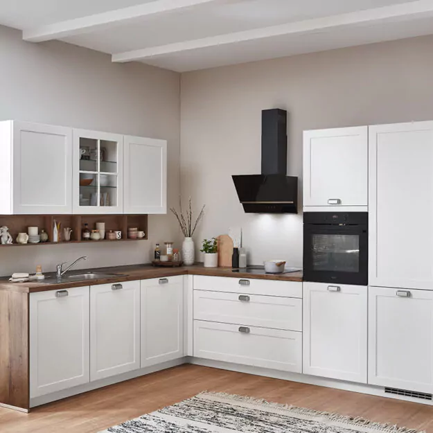 Weiße Landhausküche in L-Form mit dunkeler Holzarbeitsplatte.